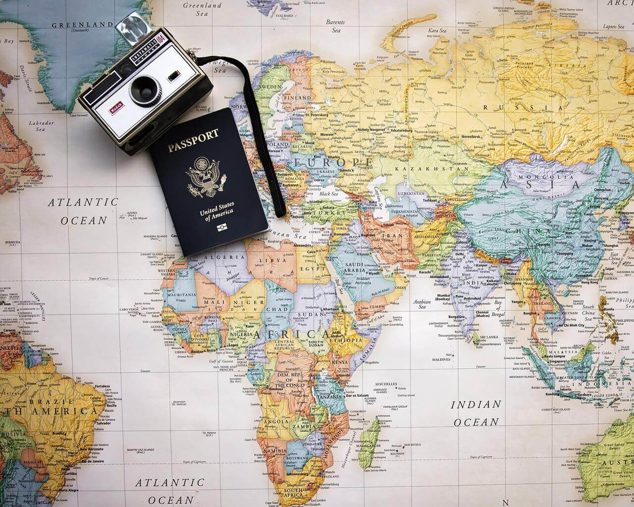 ＊ 世界地図の上にコンパクトカメラとパスポートが載せられている画像