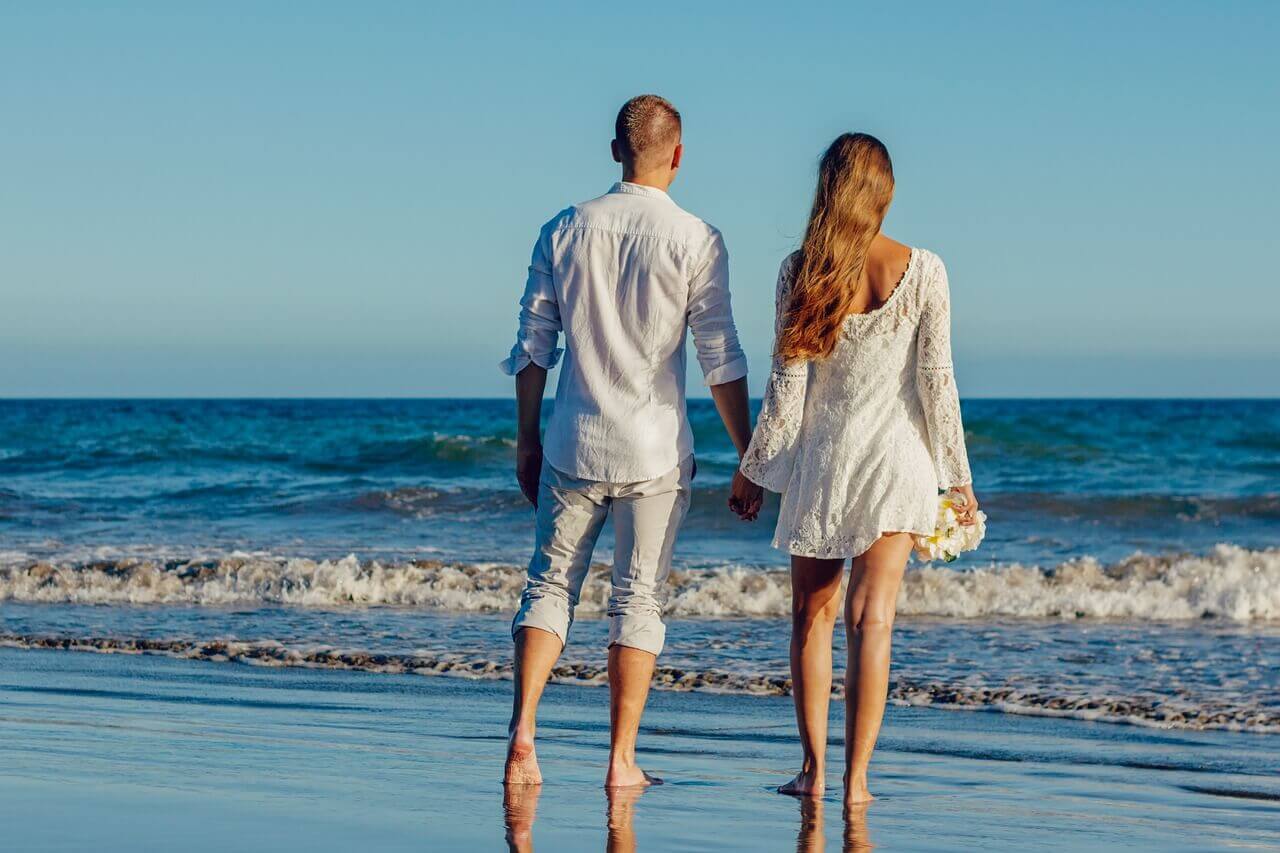 リゾートビーチで手を繋いで佇む新婚カップル