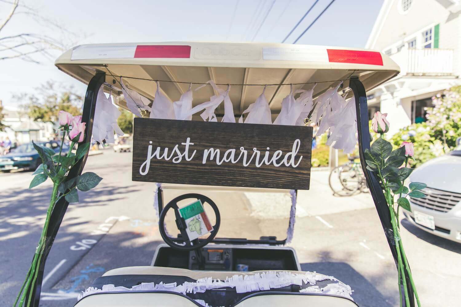 just marriedと書かれた木製看板が吊るされ、花やレースで飾られたゴルフカート